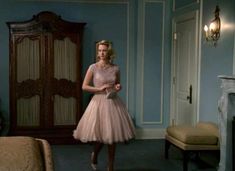 a woman in a pink dress standing next to a bed