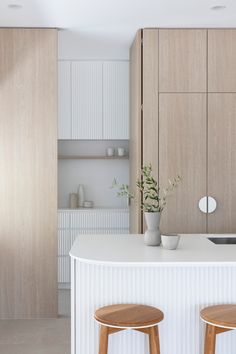 two wooden stools sit at the counter in this modern white and wood kitchen area