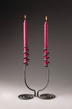 two pink candles sitting next to each other on top of a metal stand with one candle in the middle