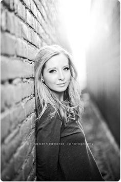 black and white photograph of a woman leaning against a brick wall