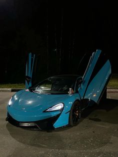 a blue sports car parked in a parking lot at night with its doors open and it's door opened