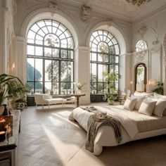 an elegant bedroom with large arched windows and white furniture, along with potted plants