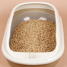 a cat litter box filled with brown and white grains on top of a pink surface