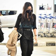 a woman wearing a face mask and black jumpsuit is walking down the street with her hand in her pocket