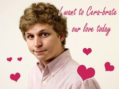 a man with curly hair wearing a pink shirt and hearts on the wall behind him