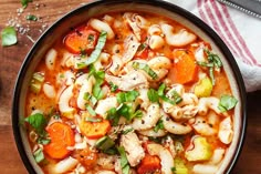 a bowl filled with pasta and vegetables on top of a wooden table next to a spoon