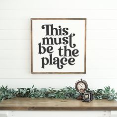 this must be the place sign above a mantle with a clock and greenery on it