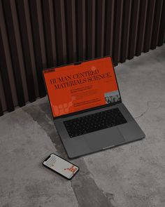 an open laptop computer sitting on top of a cement floor next to a cell phone