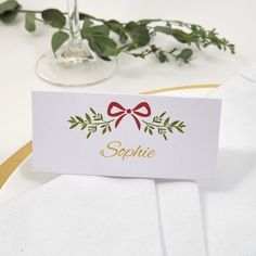 a place card with a bow on it sitting next to a wine glass and greenery