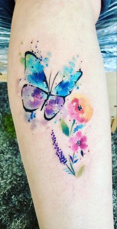 watercolor tattoo on the leg of a woman with flowers and a butterfly painted on it