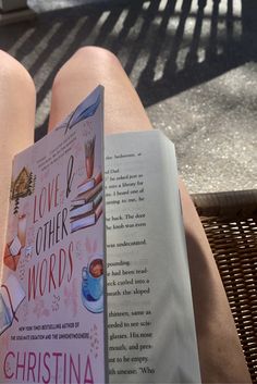 a person sitting on a bench reading a book about love and other words with their legs crossed