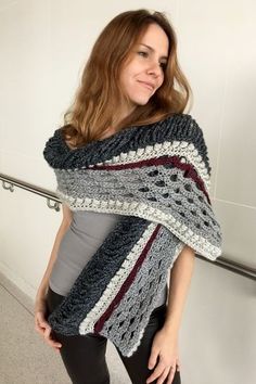 a woman wearing a gray and red crochet shawl standing in front of a white wall