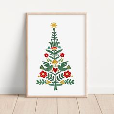 a christmas tree with flowers and leaves on it in a wooden frame against a white wall