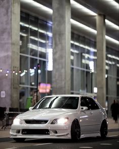 a white car parked in front of a tall building at night with its lights on