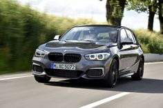 the front end of a silver bmw car driving down a road with trees in the background