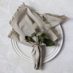 a white plate topped with two napkins covered in green leaves and flowers on top of it