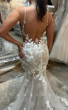 the back of a woman's wedding dress with white flowers on it, in front of a mirror