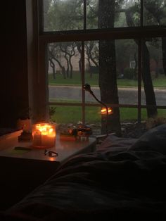 two candles sitting on a table in front of a window with the view of trees outside