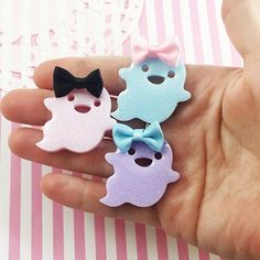 hand holding three small plastic ghost pins with bow ties on them, one in the shape of a cat