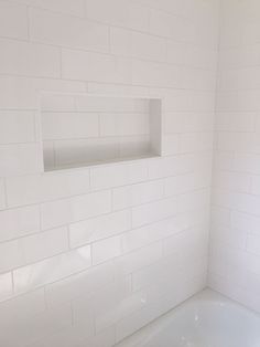 a white bath tub sitting under a window next to a toilet paper dispenser