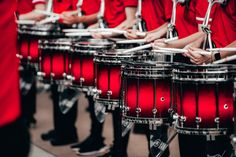 the drums are lined up and ready to be played by people in red shirts with black pants