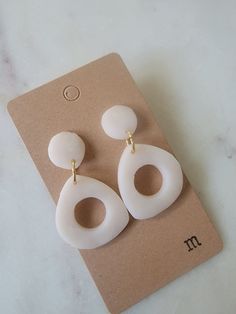 pair of white earrings sitting on top of a piece of brown paper next to a card