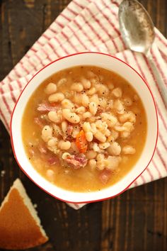 a bowl of beans and ham soup with a spoon next to it on a red and white towel