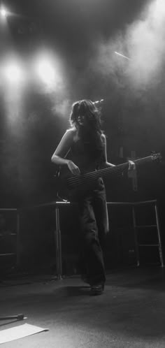 black and white photograph of woman playing bass guitar in front of spotlights on stage