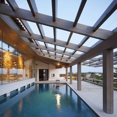 an indoor swimming pool with wooden pergolated roofing and glass doors on the side