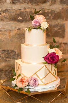 a three tiered wedding cake with pink and white flowers on top sits on a gold tray