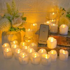 many lit candles sit next to each other in front of a cell phone and flowers