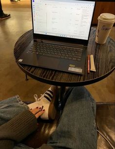 a laptop computer sitting on top of a wooden table next to a person's legs