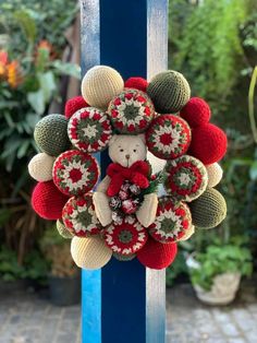 a knitted wreath with a teddy bear in the center on a blue pole outside