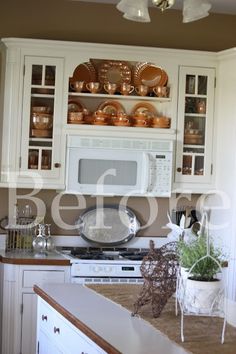 a kitchen with white cabinets and lots of dishes on top of the cupboards in it