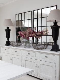 a white dresser topped with vases filled with flowers next to two lamps and a mirror