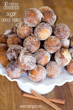 powdered sugar covered donuts on a white plate with cinnamon sticks in the background