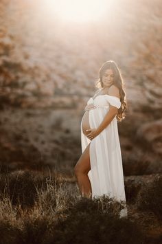 a pregnant woman in a white dress poses for a photo with the sun behind her