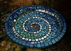 a circular blue and white mosaic design on top of a rock in front of some flowers