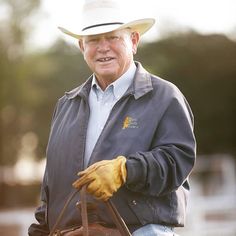 an older man wearing a cowboy hat and holding a brown leather bag in his right hand