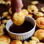 a person dipping some food into a small bowl on top of other baked goods in front of them