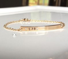 "Beautiful slender gold nameplate bracelet with 2 petite white diamond czs surrounding your intials. I hand stamp the initials and hand drill and set each stone. This is a delicate everyday gold bracelet that is a great gift for you, your friends or family! 14 k gold fill is used for the chain, bar and spring ring clasp. Gold bar dimensions: 3mm x 35mm You can have up to 5 characters stamped on this bracelet. Bracelet Sizing In order to get a nice fit, I recommend measuring the circumference of Everyday Gold Bracelet, Bar Bracelet Personalized, Diamond Bar Bracelet, Lingot D'or, Nameplate Bracelet, Custom Engraved Necklace, Gold Bar Bracelet, Handwriting Jewelry, Flower Charm Necklace