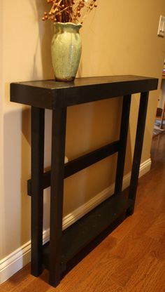 a vase sitting on top of a wooden table in front of a wall and hardwood floor