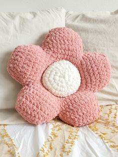 a pink crocheted flower pillow sitting on top of a bed