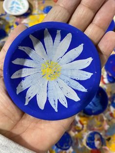 a hand holding a blue and white flower in it's left palm, with paint splatters all over the background