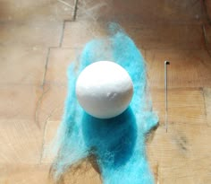 a wool ball sitting on top of a wooden floor next to a needle and thread