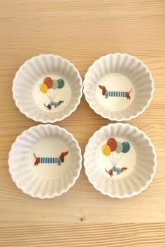 four plates with dogs and balloons on them sitting on a wooden table top next to each other