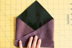 someone is making an origami envelope out of purple paper and black construction paper