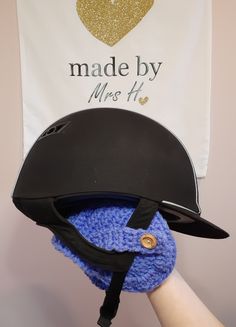 a person wearing a hat and holding a crocheted blue mitt in front of a white banner