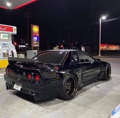 a black car is parked in front of a gas station at night with its hood up