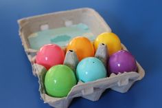 an egg carton filled with colored eggs on a blue tableclothed surface,